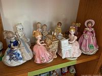 Group photo showing 8 ceramic music boxes and figurines including girls playing cello, piano, and harp, plus Victorian lady figurine