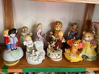 Front view of 10 of the ceramic music boxes, showing children on globe, teddy bears, and girls holding flowers and dogs