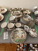 Photo showing an array of matching cups, bowls, saucers, creamers and plates featuring transferware with hunter and rural landscape designs.