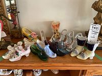 Wide view showing multiple porcelain and glass shoe and boot figurines arranged on a wooden surface