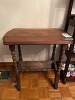Front view of the wooden side table showing turned legs and lower magazine holder shelf.