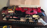 Mismatched Tonka toy vehicles including fire truck with ladder, paramedic pickup, truck cab, race car, dune buggy and tow truck shown together with ruler for scale.