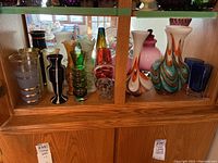 Front view of assorted art glass vases on wooden shelf showing overall lot contents.
