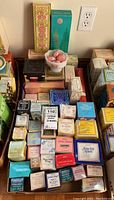 Overview of multiple boxed vintage Avon colognes, creams, and soaps arranged on table.