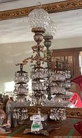 Front view of the lamp showing three tiers of crystal prisms, brass frame and cut glass globe top.
