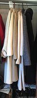 Seven women's coats hanging in a closet showing varied neutral colors and styles