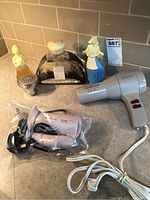 Lot overview with both blow dryers, Philips travel dryer in plastic, and decorative bottles on countertop.