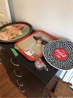 Three Coca-Cola trays and a small plastic container holding a yo-yo on a dresser