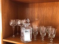Overall view of the decanter with stopper and seven crystal stemmed glasses on wooden shelf