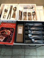 Two sets of cutlery arranged in white and black trays with a Christmas cooking cookbook beside them