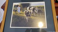 Framed print showing a girl in a white dress tending to a group of black and white cows in an outdoor rural setting.