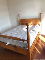 Wooden 4 poster bed frame with mattress installed in a well-lit room, showing the entire bed and mattress surface.