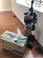 Eureka upright vacuum cleaner next to a Rumidifier humidifier box on wooden floor.