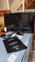 Photo showing the Insignia 24-inch LED TV/DVD combo on a white table with power adapter and manuals visible.