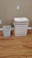 Photo showing both the white wicker laundry hamper with lid and matching waste basket side by side on floor.