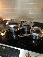 Three stainless steel Lagostina pots with lids on stovetop, showing different sizes and handles.