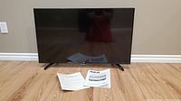 RCA 40 inch TV shown standing on hardwood floor with instruction manual and remote placed in front.