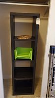 Tall black shelf with cubby holes, wire basket on top shelf, green basket on middle shelf