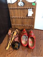 Wooden spoon display shelf standing against wall, with wooden shoes and roller skates in front on wooden floor