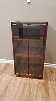 Front view of stereo stand showing wood grain finish and two glass doors with metal latch.