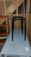 Two black stools stacked on top of each other seen from side angle, showing height and legs.