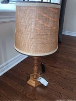 Full view of the wooden table lamp showing the fabric shade and wooden turned base on hardwood floor near window.