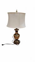 Full view of brass table lamp with fabric shade and black cord, standing upright
