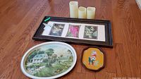 Overview photo showing framed flower artwork, three battery candles, and two decorative trays on wooden flooring.