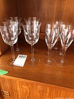 Crystal wine glasses with etched floral designs and clear glass champagne flutes arranged on wooden shelf.
