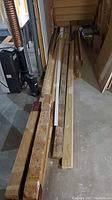 Various lengths of wooden boards including 2x4s and 2x6s laid on a basement floor near a furnace system