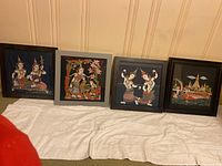 Four framed Asian art pieces displayed side by side with cloth under them. Each features traditional Asian art imagery.