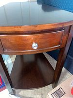 Close-up photo showing the drawer front with metal pool knob and bottom curved shelf, part of wooden end table.