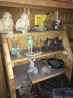 Full shelf view showcasing all garden figurines arranged on wooden shelving including frogs, birds, rabbits, cherubs, and lawn care items.