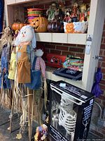 Full view of Halloween scarecrows, ceramic pumpkin, candy buckets, placemats and boxed skeleton on shelf