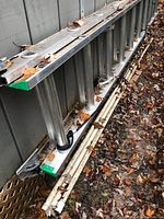 20 foot aluminum Werner extension ladder with green capped ends folded and resting against siding, leaves around.