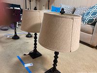Two matching table lamps with spindle wooden bases and beige fabric drum lampshades.