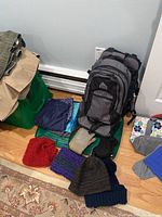 Photo showing Kelty kids backpack, various knit hats, and gloves on floor near folded clothing and bags.