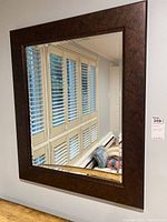 Full front view of the rectangular wall mirror showing the wide brown wooden frame and reflective glass surface.