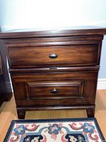 Front view of wooden nightstand showing two drawers with metal pulls and dark brown finish.
