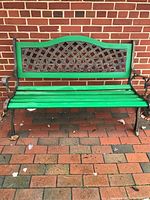 Front view of outdoor bench with green wooden slats and iron lattice backrest.