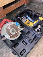 DeWalt drill, Milwaukee circular saw, and drill bits in open plastic cases, tools resting on concrete floor.