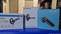 Photo showing three boxed single-ear handsfree Bluetooth communicators: HSP-B6, HonShoop, and New Bee LC-D30 models.