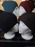 Photo showing four knitted toques on mannequin heads in teal, red, black, and brown colors.