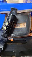 Slonik headlamp resting on carrying pouch with visible branding and adjustable strap.