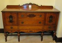 Front view of the 1930's walnut sideboard showing cabinetry, drawers, decorative hardware, and carved backsplash.