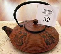 Angled front view of the antique Japanese cast iron teapot showing textured brown exterior with raised characters, black handle, and spout.