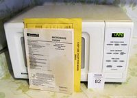 Front view of Kenmore microwave oven with instruction manual displayed in front showing brand and model info.