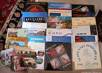 Top view of approximately 25 Slovenian vinyl records arranged in a grid showing various album cover artwork and titles including choir ensembles, pastoral scenes, and artistic portraits.