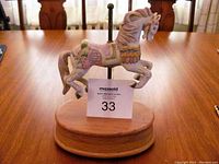 Front angle of musical carousel horse figurine on wooden base with auction label in front