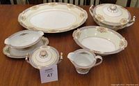 Full overview of all eight Noritake serving pieces arranged on a wooden table showing platter, bowls, creamer, sugar bowl, casserole with lid, and gravy bowl.